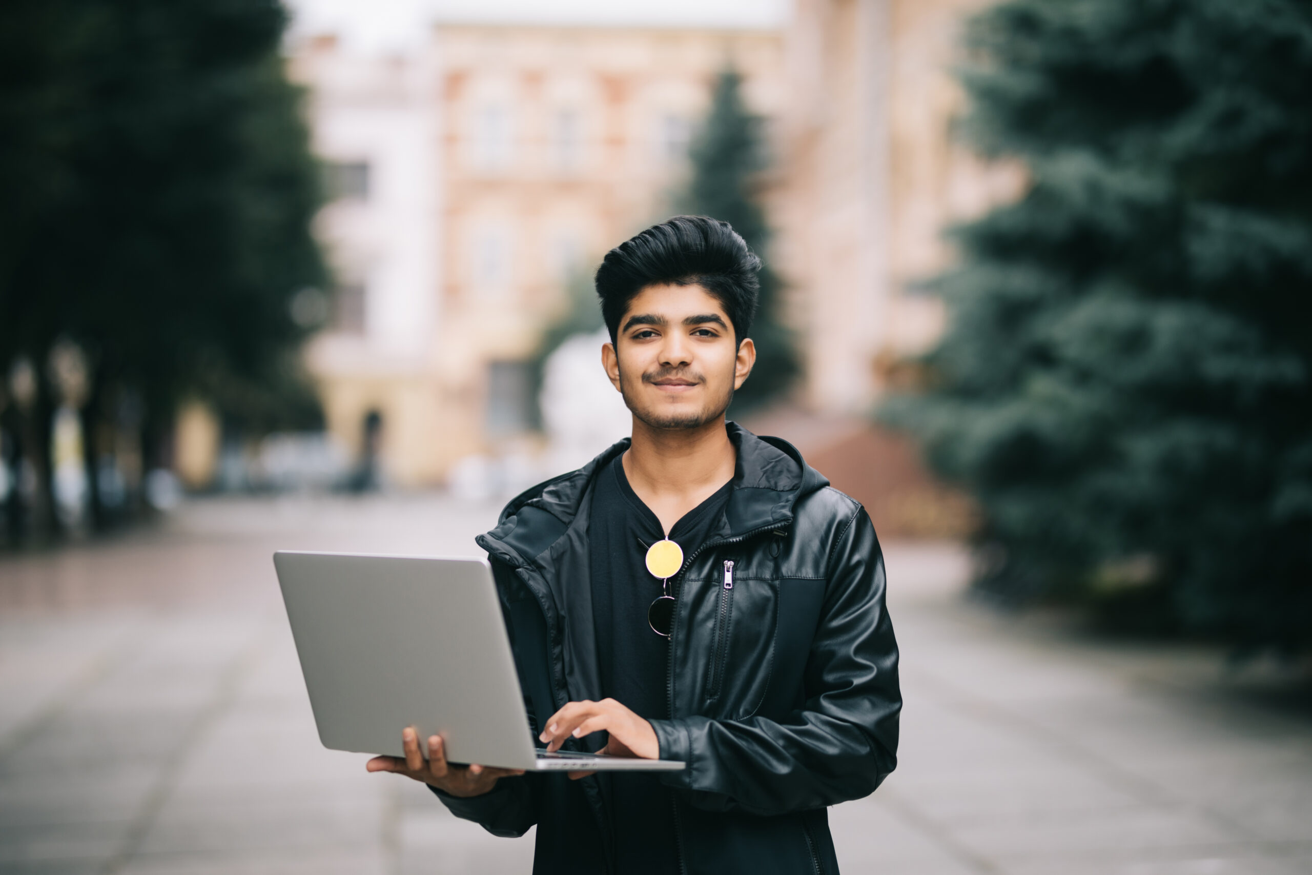 Young indian man standing outdoor with laptop in front of business building